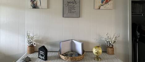 Una habitación con una pared blanca con paneles, una cita enmarcada y dos obras de arte enmarcadas que representan una libélula y un pájaro. Hay una pequeña mesa con un globo terráqueo, una cesta y un letrero que dice "THANKFUL, GRATEFUL, blessed".