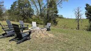 Un foyer extérieur entouré de quatre chaises Adirondack, le tout installé dans un espace extérieur verdoyant.