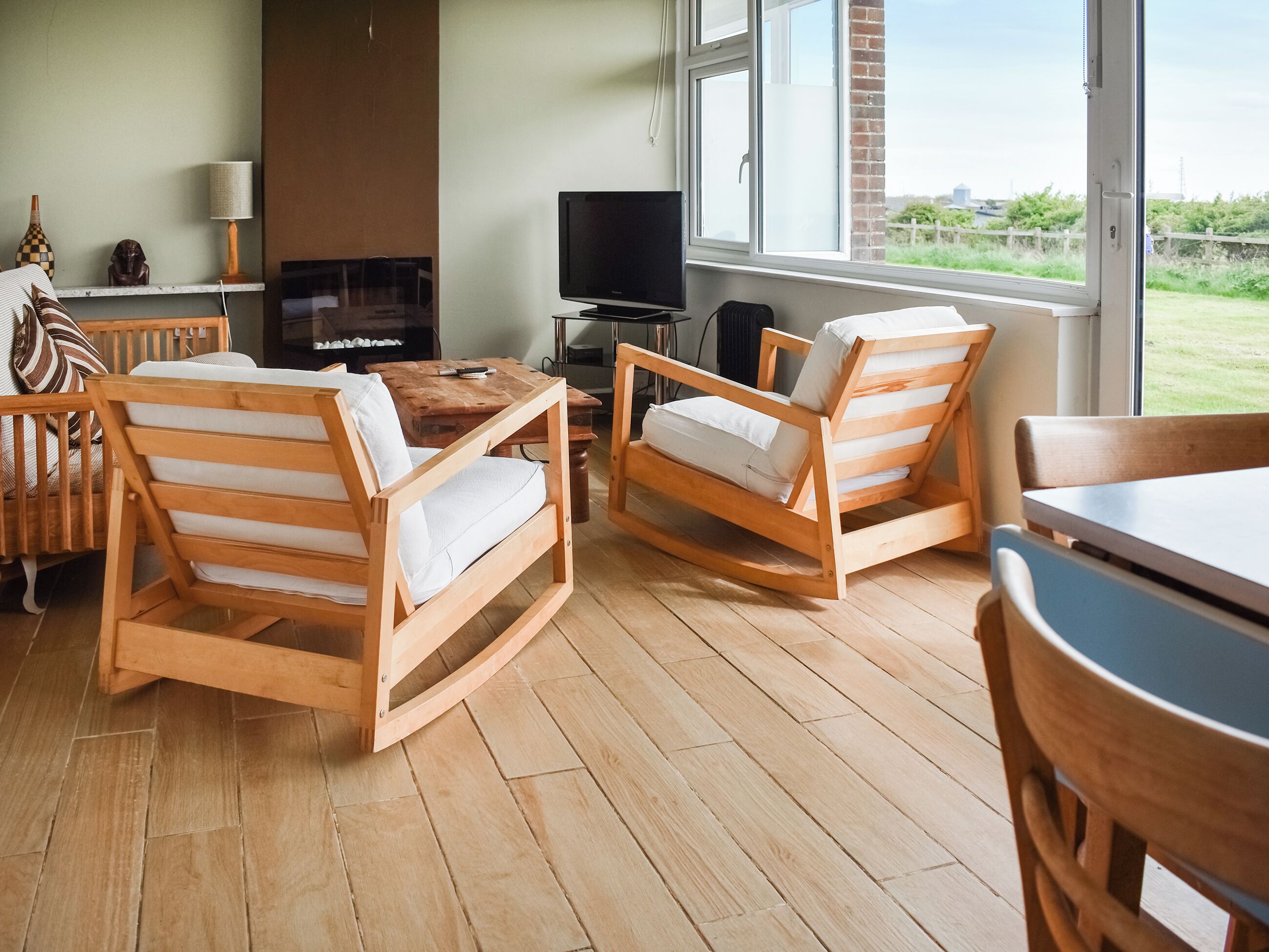 A cozy living room with wooden furniture, a fireplace, and a large window offering a view of the outdoors.