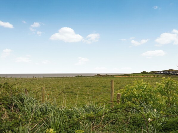 A grassy field with a wooden fence and a distant view of a body of water. - 2 bedroom accommodation in Mundesley (Mundesley)