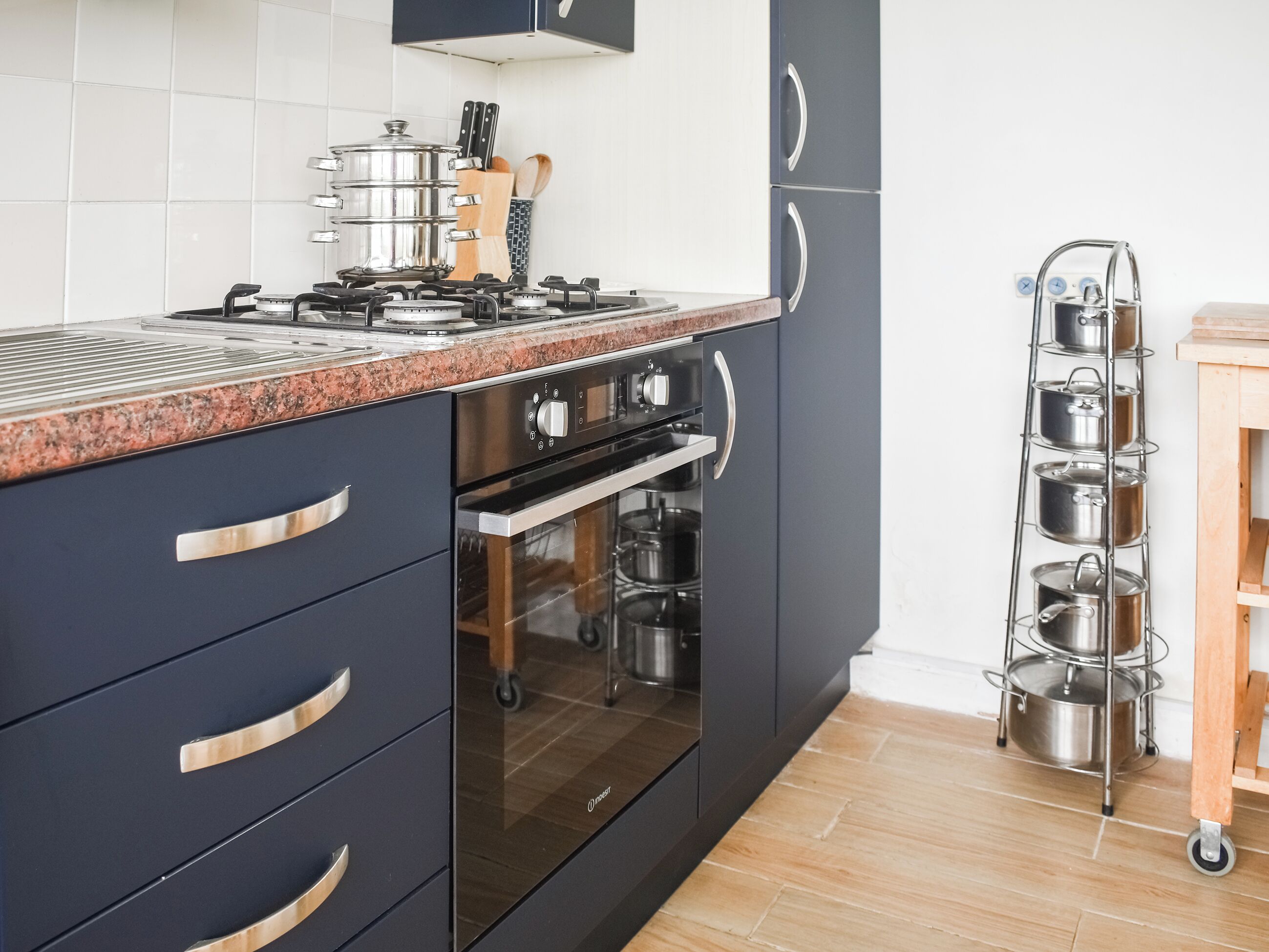 Une cuisine moderne avec des meubles de rangement aux couleurs sombres, une cuisinière à gaz, un four et un porte-casseroles.