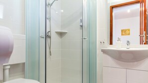 Un baño con ducha de vidrio, inodoro y lavamanos con espejo.
