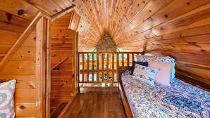 Una cabaña de madera con un dormitorio en el altillo, una escalera y una chimenea de piedra.