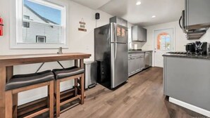 Una cucina moderna con frigorifero in acciaio inossidabile, tavolo da pranzo in legno con panche e una finestra con persiane.