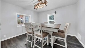 Una sala da pranzo con tavolo e sedie in legno, un lampadario a soffitto e finestre con vista sull'esterno.