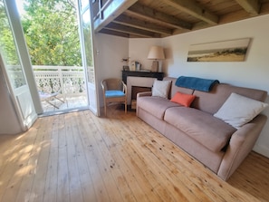 A cozy room with a wooden floor, a sofa, a chair, a lamp, and a painting on the wall.