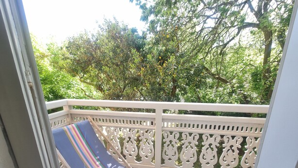 Un balcon avec une chaise à rayures, une balustrade blanche et de la verdure en arrière-plan.