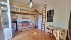 Une pièce avec un lit superposé, une échelle en bois, une table recouverte d’une nappe, un canapé et une lampe.