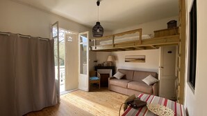 Une pièce avec un plancher en bois, un canapé, une table recouverte d’une nappe à rayures, un luminaire suspendu et un lit superposé.