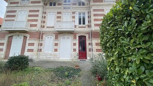 Un bâtiment à deux étages avec une porte rouge, des volets blancs et une enseigne sur laquelle on peut lire « LES ÉRABLES ».