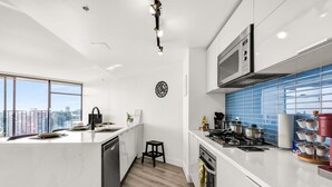 Una cocina moderna con una isla grande, armarios blancos, un salpicadero azul y vistas a la ciudad a través de amplias ventanas.