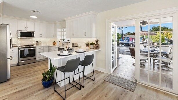 A modern kitchen with white cabinets, a central island with bar stools, a microwave, and an oven.