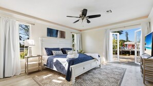 A bedroom with a bed, a ceiling fan, a TV, and a view of the outdoors.