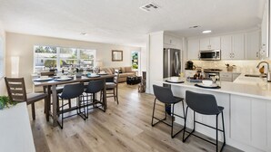 A modern kitchen with white cabinetry, a central island, and a dining area with a table and chairs.