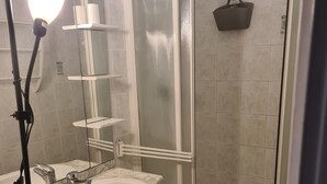 Un bany amb un rentapousa blanc, un mirall, una dutxa amb porta de vidre i un suport de tovalloles.