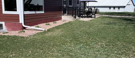 A single-story house with a red exterior and a white trim, a front porch with a black railing, and a small patio area with outdoor furniture.