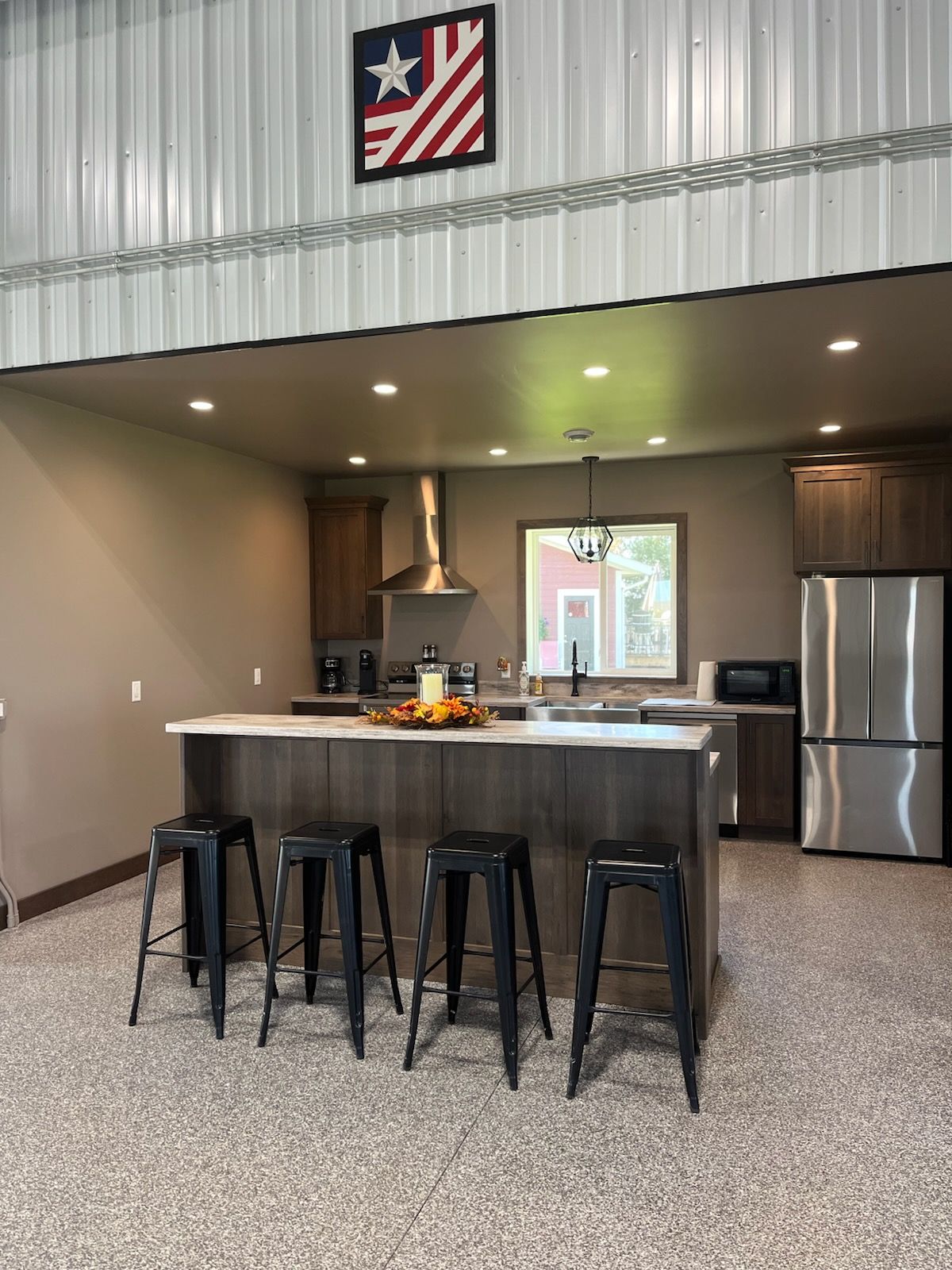 A modern kitchen with a central island, bar stools, stainless steel appliances, and a flag decoration.