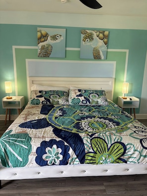 Un lit recouvert d’une couvre-lit à motifs floraux, deux tableaux représentant des tortues de mer accrochés au mur, et des lampes de chevet de chaque côté.