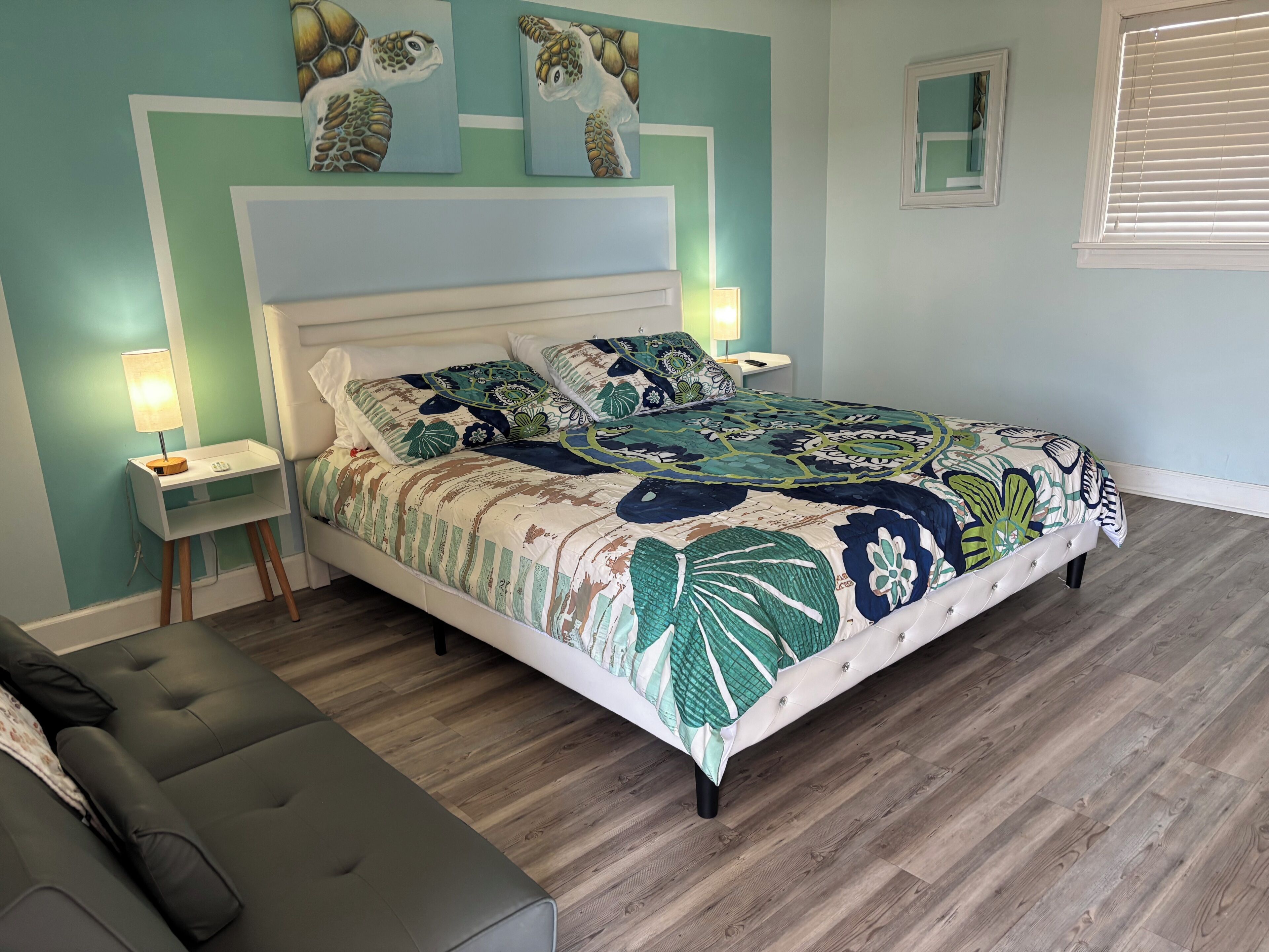 Um quarto com cama, mesas de cabeceira, abajur, um banco e obras de arte na parede.