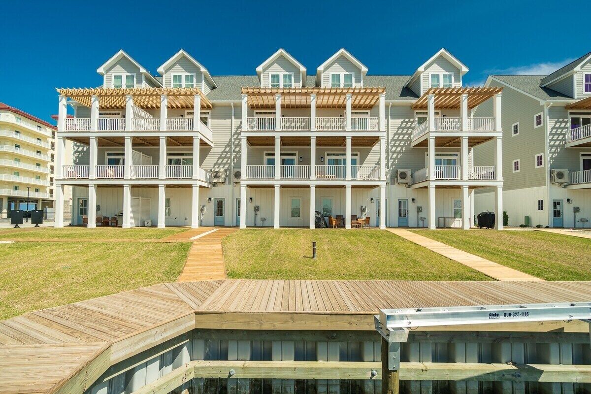 A beachfront hotel with multiple balconies, a wooden deck, and a clear sky.