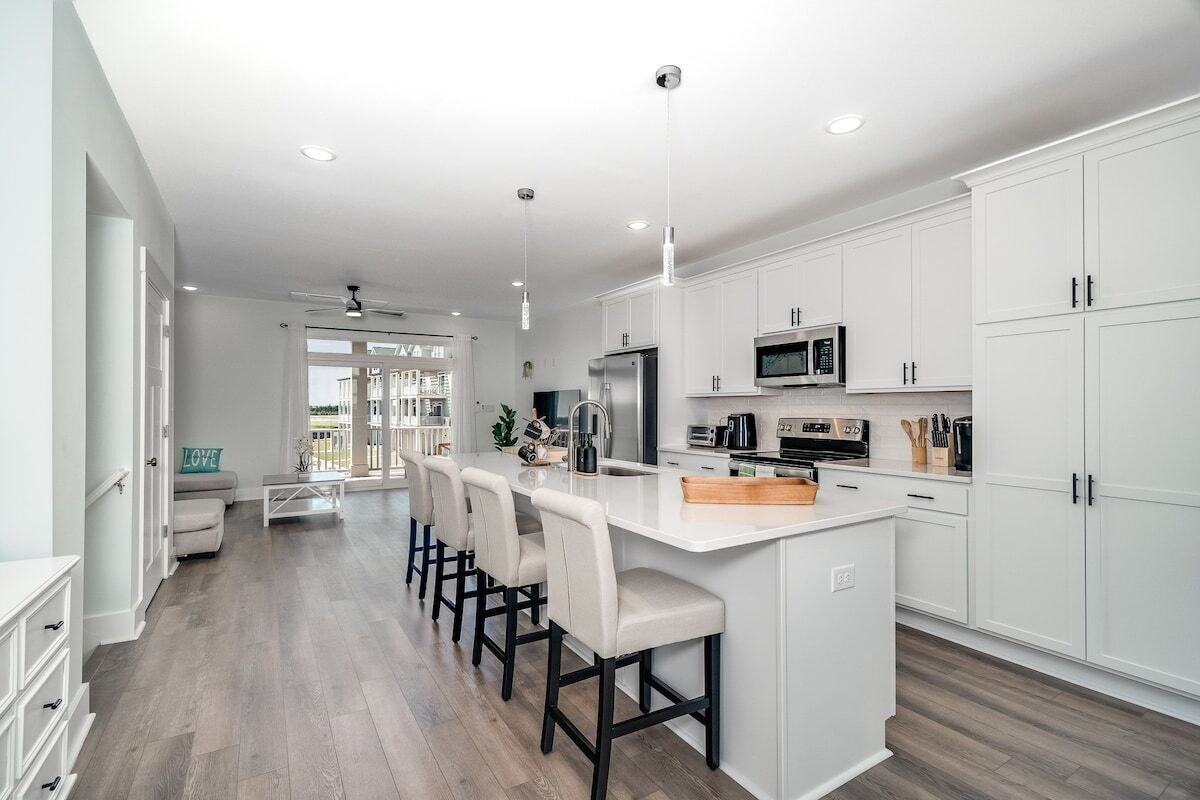 A modern kitchen with white cabinets, a central island with bar stools, and a view to the outside.