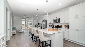 A modern kitchen with white cabinets, a central island with bar stools, and a view to the outside.