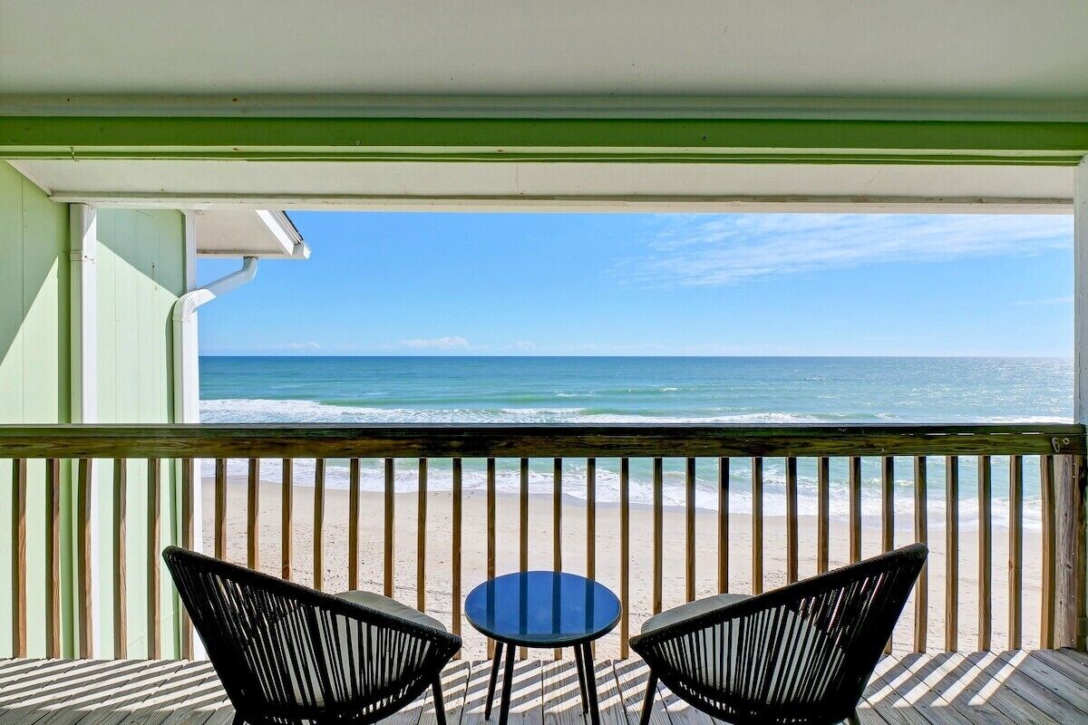 Uma varanda com vista para o oceano, duas cadeiras e uma mesa pequena.