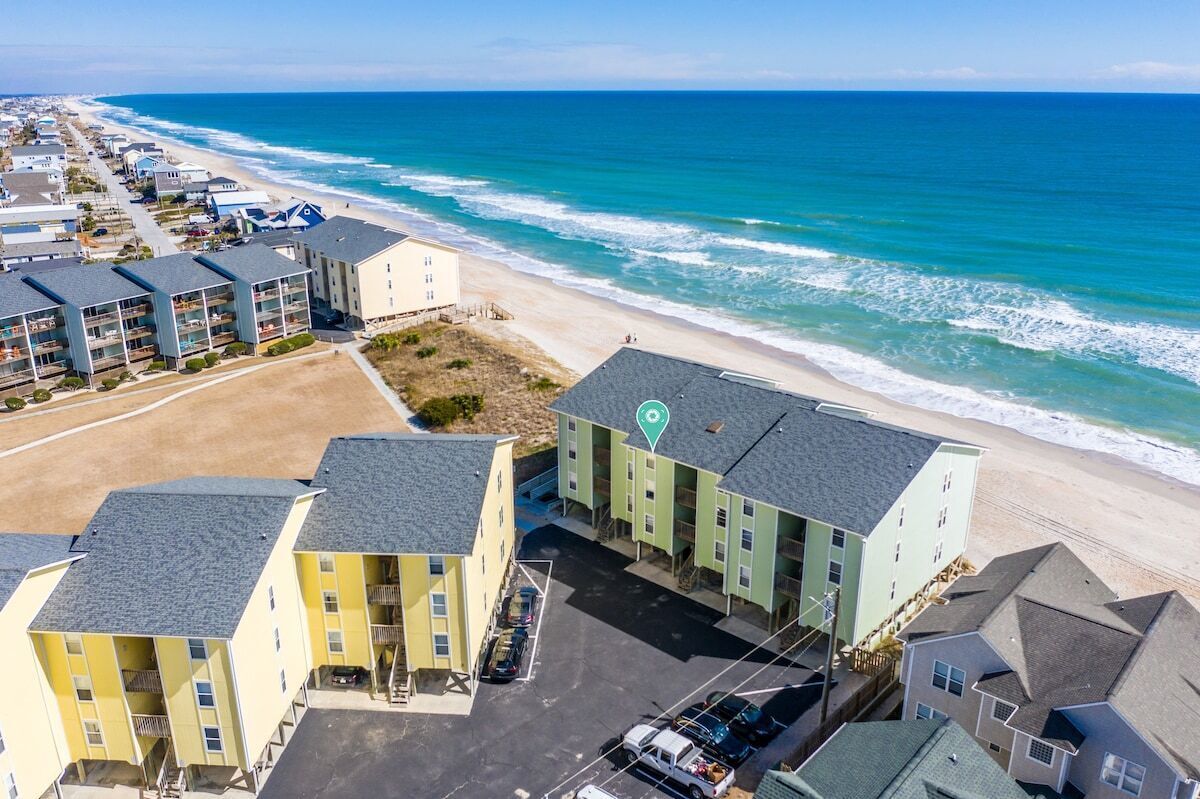 A coastal hotel with multiple buildings, a parking lot, and a beach view.
