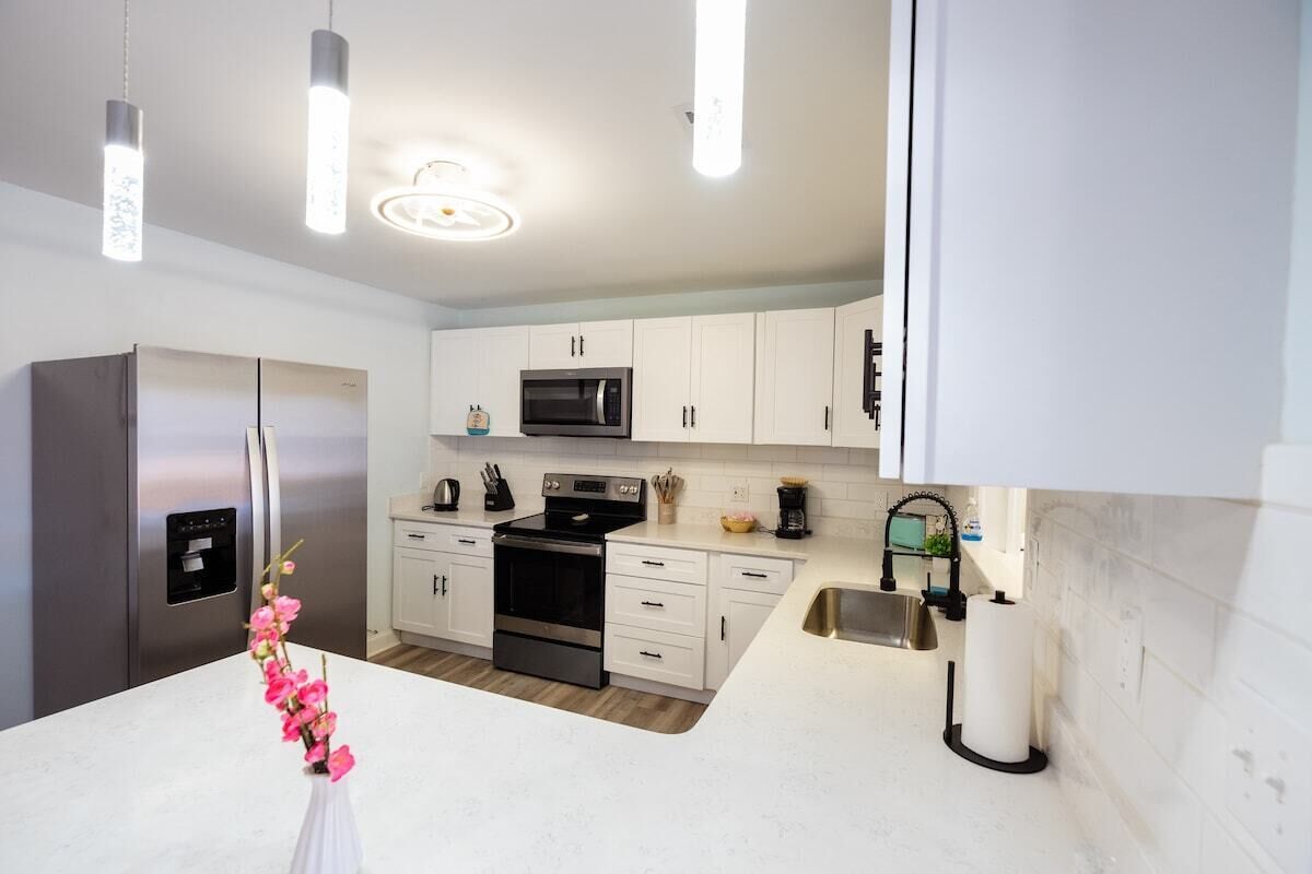 A modern kitchen with white cabinets, stainless steel appliances, and pendant lighting.
