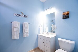 A bathroom with a blue wall, a white sink, a toilet, and two towels hanging on hooks. - Emily - Offshore Beach Club (Buxton)