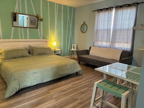 A room with a bed, a sofa, a small table, and a mirror.