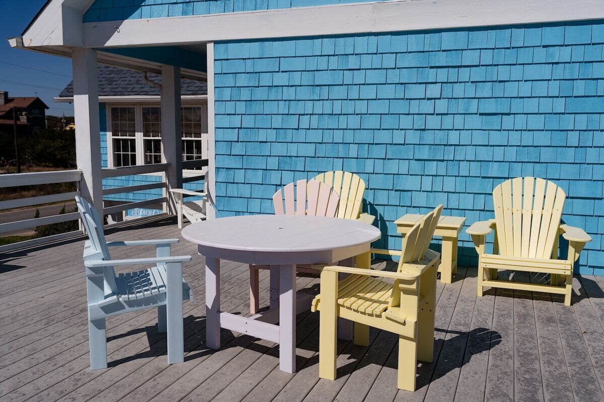 Eine Holzterrasse mit einem runden Tisch und vier Adirondack-Stühlen.