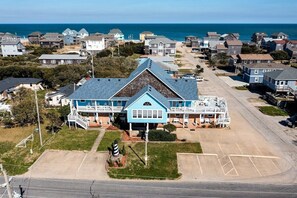 A coastal building with a prominent blue roof and a white facade, surrounded by residential houses and a parking lot. - Andrew - Offshore Beach Club (Buxton)