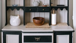 A kitchen with a black and white cabinet, a wooden bowl, a white pitcher, and a set of glasses on the shelves.