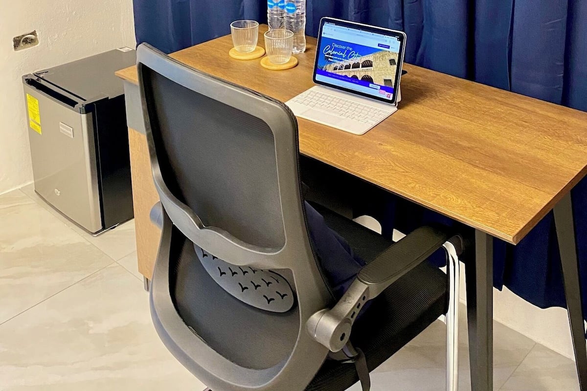 A hotel room with a wooden desk, a laptop, two water bottles, and a television on the wall.