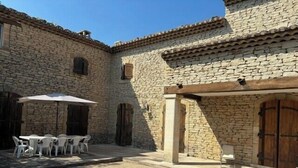 A courtyard with stone walls, a wooden door, and a table with chairs under an umbrella. - Mas in Gordes with swimming pool (Gordes)