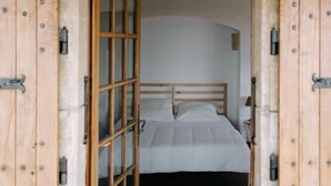 A bedroom with a wooden door, a bed with white bedding, and a stone wall. - Mas in Gordes with swimming pool (Gordes)