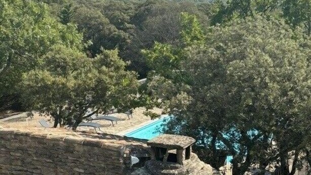 A stone structure with an arched entrance, surrounded by trees and a clear view of a swimming pool in the background. - Mas in Gordes with swimming pool (Gordes)