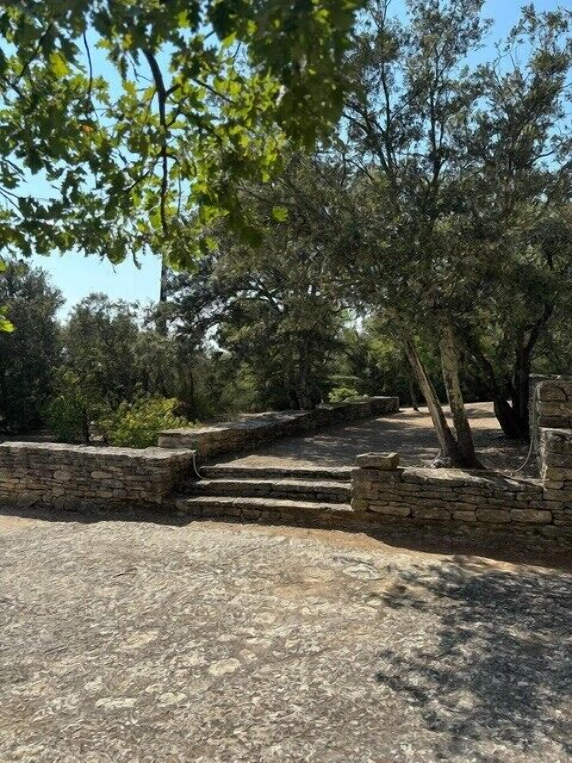 A stone staircase leading up to a stone wall, surrounded by trees and greenery.
