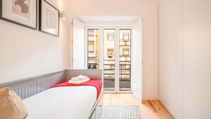 Une chambre d’hôtel étroite, avec un lit, une petite fenêtre et une vue sur un immeuble.