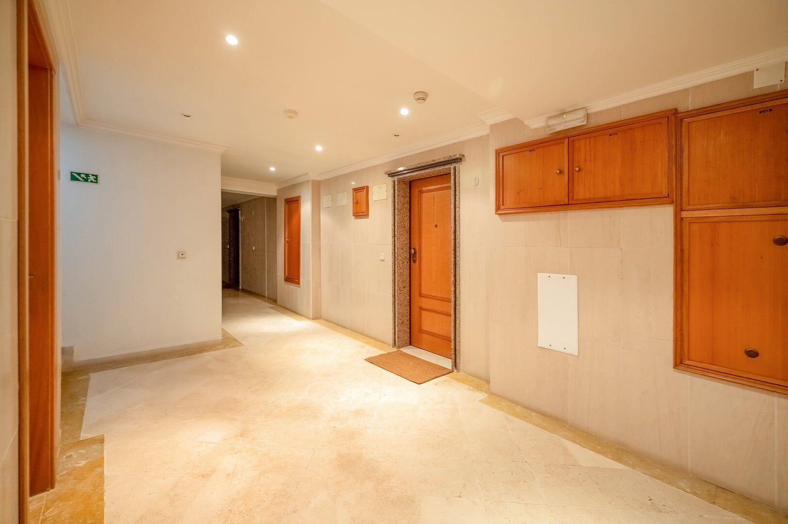A hallway with wooden doors, a doormat, and a sign indicating an exit.