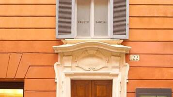 Facciata di un edificio con un'ampia porta in legno a due battenti, una piccola targa con il numero 122 e due finestre con persiane etichettate 'FAUSTO' e 'SANTINI'.