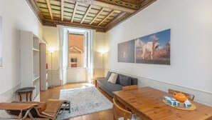 A cozy living room with a wooden dining table, a sofa, and a view of a desert landscape through the open door. - Frattina Atmosphere apartment (Rome)