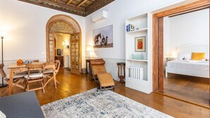 A room with a wooden dining table, a sofa, a chair, a radiator, a bed, and a ceiling with intricate designs. - Frattina Atmosphere apartment (Rome)