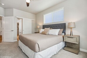 A bedroom with a large bed, a nightstand, a lamp, a window with blinds, and a closet. - Pure Suites Lux 2 Bed Desert Ridge 2 Pools Gym (Phoenix)