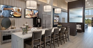A modern kitchen with a large island, bar stools, and a flat-screen TV.