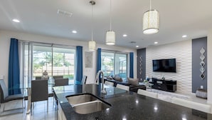 A modern kitchen with a central island, a dining area with chairs, and a living area with a sofa and TV. - Beautiful and Cozy Home at Sonoma Resort (Kissimmee)