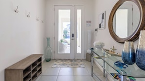 A hallway with a wooden bench, a glass display case with decorative items, a large mirror, and a door leading to an outdoor area. - Beautiful and Cozy Home at Sonoma Resort (Kissimmee)