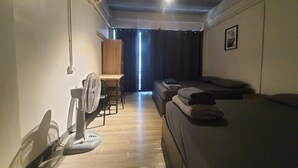 A room with a bed, a desk, a chair, and a standing fan.