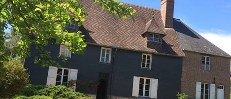 Een huis met twee verdiepingen, gevel van baksteen, witte luiken en een schoorsteen.
